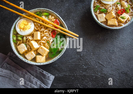 Soupe ramen japonais avec du tofu et des oeufs sur pierre sombre arrière-plan. La soupe miso avec des nouilles ramen et le tofu dans un bol en céramique, asiatique traditionnelle. Banque D'Images