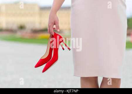 Une femme élégante tenue rouge de luxe hautes chaussures de talon dans sa main Banque D'Images