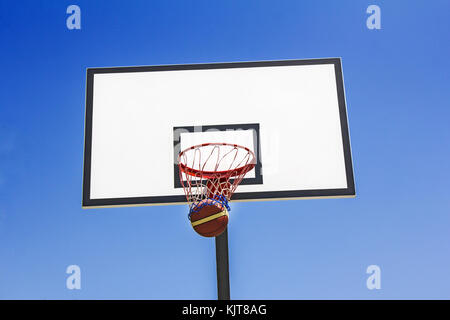 Balle de basket-ball le panier dans le fond de ciel bleu Banque D'Images