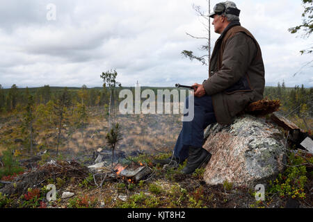 Moosehunter assis sur une pierre avec un feu en face de lui tenant un fusil, photo du nord de la Suède. Banque D'Images