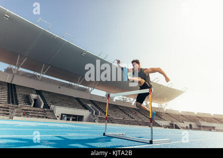 Runner sautant par-dessus un obstacle lors d'événements d'athlétisme. L'exécution d'un athlète course de haies dans un stade. Banque D'Images