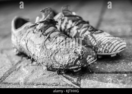 Image en noir et blanc d'une paire de chaussures de football junior très couvertes de boue Banque D'Images