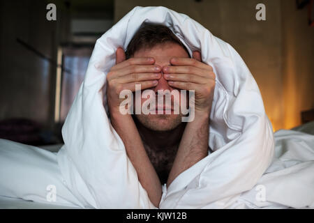 Le fatigué caucasian man se coucha sur le lit et couvrir le visage avec les bras. Banque D'Images