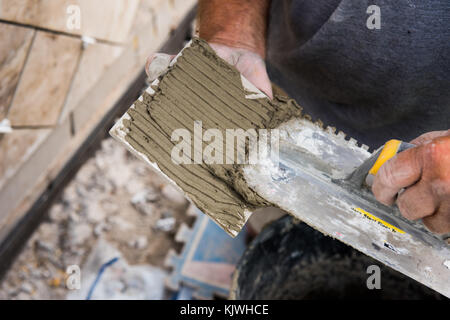 Le mortier appliqué à une tuile avec une truelle à gorge pour elle de s'en tenir à la surface de montage. Banque D'Images