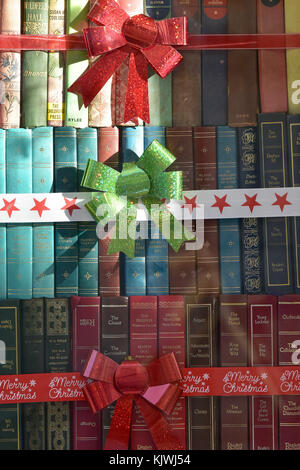 Certains vieux ou ancien joliment livre dans le cuir et tissu dans la fenêtre d'une librairie avec des décorations de Noël en rouge et vert des arcs et des étoiles Banque D'Images