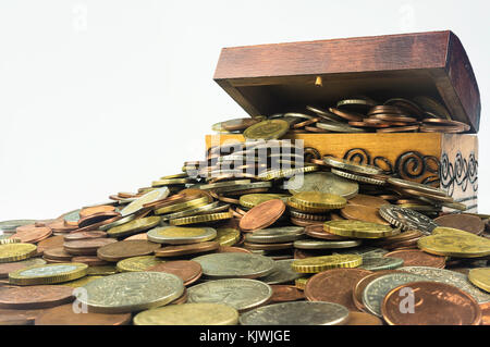 Un petit coffre au trésor en bois qui regorge de pièces sur un fond blanc. Composition isolée qui est liée à la situation économique et financière Banque D'Images