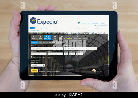 Un homme regarde le site Web Expedia sur son iPad tablet device, tourné contre une table en bois page contexte (usage éditorial uniquement) Banque D'Images