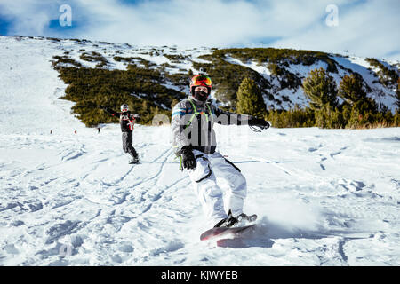 Jeune homme snowboard manèges et profiter d'une journée d'hiver ensoleillée sur les pentes des montagnes. Banque D'Images