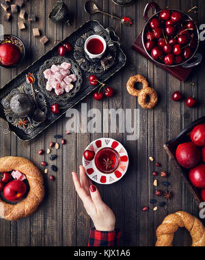 Thé rouge de femme près de loukoums rahat lokum, simits et fruits sur table en bois Banque D'Images