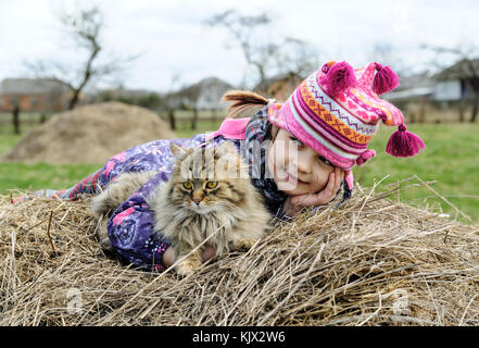 La fille avec le fluffy chat est sur une botte de foin. Banque D'Images