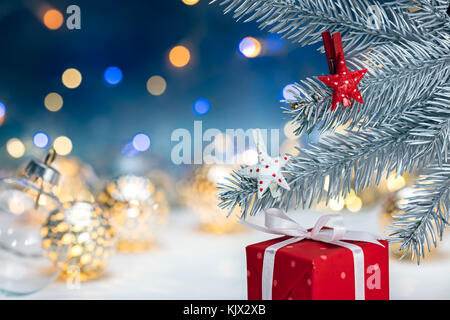 Sous Boîte cadeau rouge christmas sapin avec des décorations de la direction générale contre l'arrière-plan Lumières floues Banque D'Images