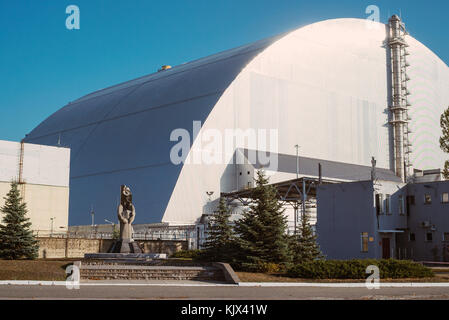 Un dôme de protection au-dessus du réacteur nucléaire de Tchernobyl car il est encore en train d'être démantelé, 30 ans plus tard. Une statue commémorative se trouve à l'avant Banque D'Images