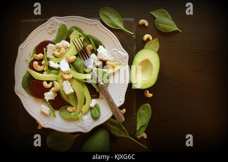 Une salade de bébés épinards sucré frais, noix, fromage feta et l'avocat. La plaque avec le tableau sombre de la salade. Vue d'en haut Banque D'Images
