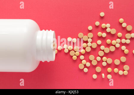 Groupe d'assorted capsules comprimés beiges. spilling out of white bouteille. fond rouge. Banque D'Images