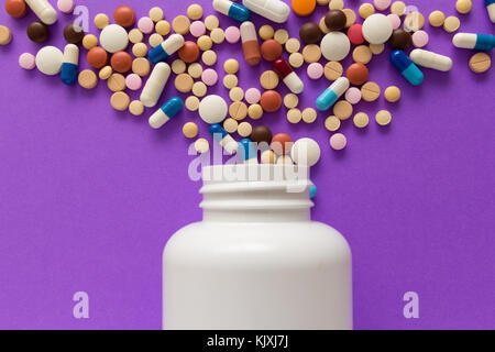 Groupe d'assorted capsules colorées. comprimés spilling out of white bouteille. violet. Banque D'Images