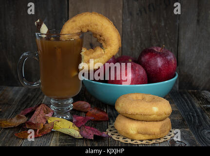 Donut sur le bord du verre de cidre mug sur feuilles d'automne et pommes rouges en bois rustique sur bol turquoise Banque D'Images