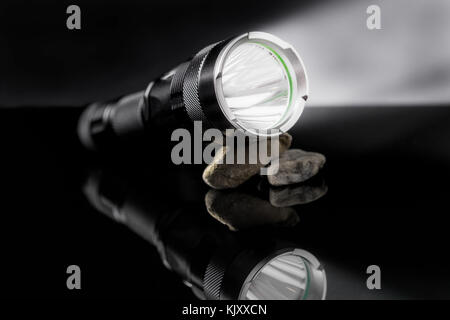 Lampe noire avec des lumières ouvrir sur des pierres mirroring sur fond noir. Utile pour l'aventure, militaire, chasse, extérieur, la protection, l'arrière-plan Banque D'Images
