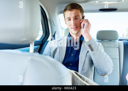 Portrait de jeune homme parlant par téléphone assis sur siège arrière de voiture de luxe, copy space Banque D'Images