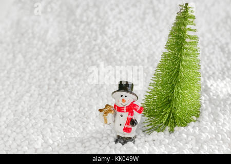 Bonhomme de neige miniature avec un cadeau s'en tient à un arbre de Noël, profondeur de champ, l'espace pour le texte. Banque D'Images