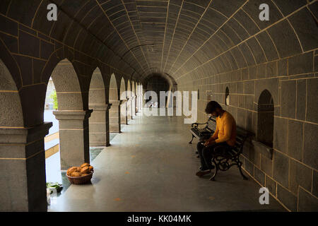 Jeune Indien habillé en orange, vérifiant son mobile assis dans le porche du temple, Vitthal Mandir, Vithalwadi, Pune Banque D'Images
