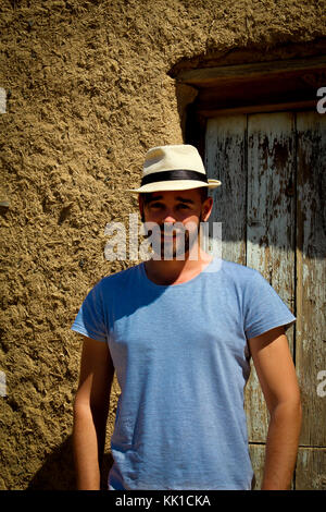 Caucasian man smiling with hat sur debout devant la porte de chambre de boue Banque D'Images