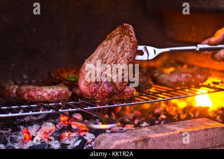 Steak avec des saucisses et du wurstel sur le feu du barbecue à charbon de bois incandescent incandescent Banque D'Images