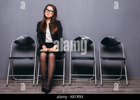 Les gens, l'emploi et le recrutement. Charmant chômeuse de verres tout sourire après avoir convaincu regardez avant d'entrevue d'emploi, assis sur une chaise Banque D'Images