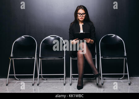 Les gens, l'emploi et le recrutement. Charmant chômeuse de verres tout sourire après avoir convaincu regardez avant d'entrevue d'emploi, assis sur une chaise Banque D'Images