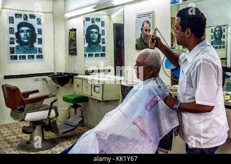 Une coiffure couper les poils à un client avec le rasoir électrique dans un magasin rempli d'affiches révolutionnaires, Vieille Havane, Cuba Banque D'Images