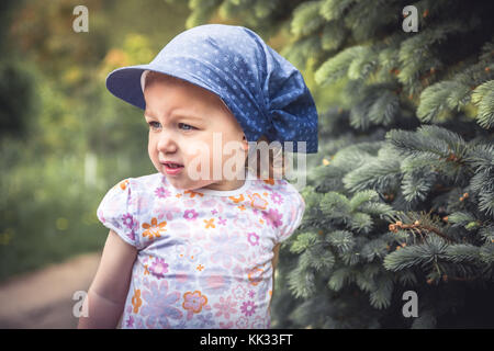 Girl portrait enfant espiègle frouned entre les sapins sur arrière-plan flou Banque D'Images