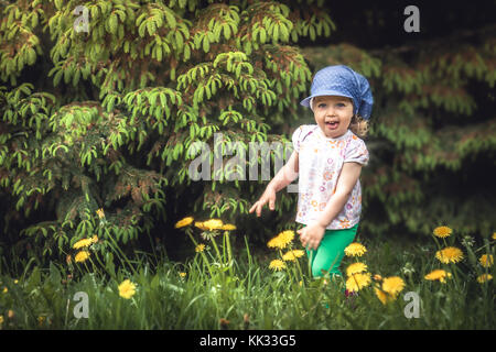 Enfant espiègle cheerful girl running on meadow entre sapins et fleurs de pissenlit pendant les vacances d'enfance insouciante heureux symbolisant Banque D'Images