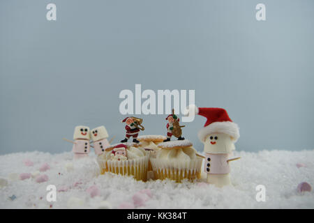 Noël Nourriture photographie image avec éponge crème gâteau fée placés dans la neige avec des guimauves en forme de bonhomme heureux et santa hat Banque D'Images