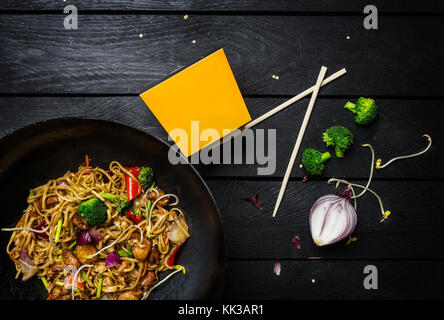 Sauté au wok, udon Nouilles au poulet et les légumes dans le wok casserole sur fond de bois noir. avec un fort pour les nouilles Banque D'Images