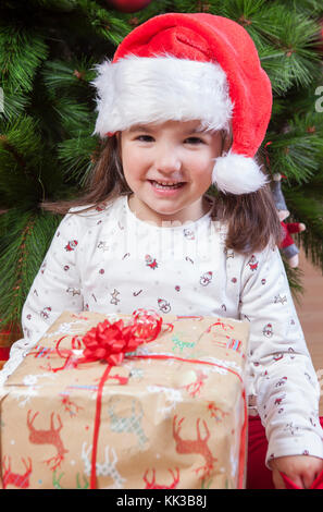 Petite fille joyeuse avec sa boîte cadeau sous l'arbre de Noël.Elle vient de trouver son présent Banque D'Images