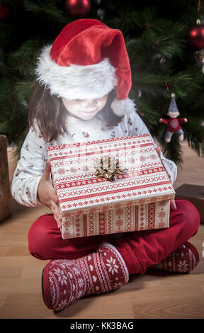 Petite fille ouvrant son cadeau à côté de l'arbre de Noël.Elle est illuminée par la brillance de la boîte Banque D'Images