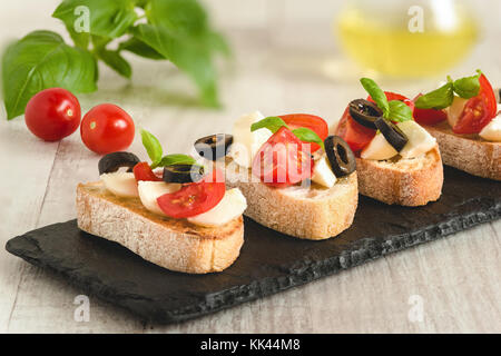 Snack avec sandwichs italiens bruschetta mozzarella, tomates et olives noires décorées par des feuilles de basilic. Banque D'Images