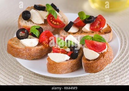 Snack avec sandwichs italiens bruschetta mozzarella, tomates et olives noires décorées par des feuilles de basilic. Banque D'Images