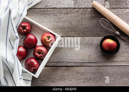 Pommes rouges bien mûrs dans le bouleau blanc le bac sur planche de bois, d'accessoires pour la cuisson et la copie de l'espace pour votre texte. Banque D'Images