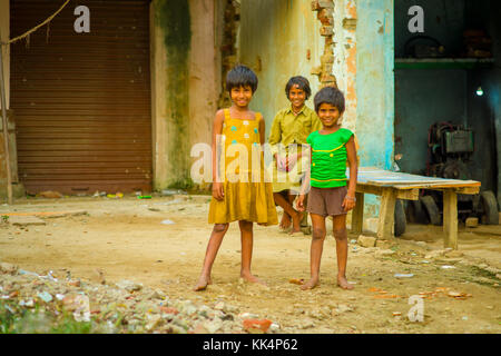 Agra, INDE - 20 septembre 2017 : portrait de l'enfant, vêtu d'un corsage et une sale jaune t-shirt vert et un pantalon marron et, sur un sol de pierres, dans la rue dans la ville d'agra en Inde Banque D'Images