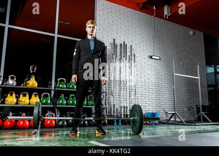 Le mec est en train de poser dans la salle de sport sur l'arrière-plan gris Banque D'Images