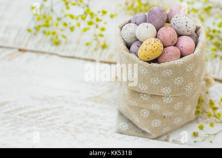 Bonbons au chocolat petit multi-couleur des oeufs de pâques en chocolat de caille en couleurs pastel , sac sur table en bois blanc fleurs de printemps jaune copie espace poste Banque D'Images