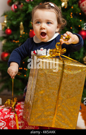 Beau Bébé fille tout-petits avec des cadeaux près de l'arbre de Noël. Banque D'Images