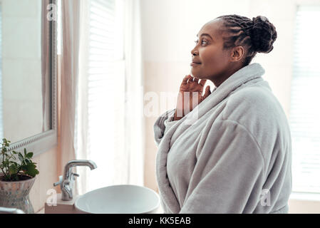 Femme africaine à la recherche de son teint dans un miroir de salle de bains Banque D'Images