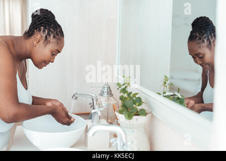 Jeune femme africaine lave son visage dans le lavabo de la salle de bains Banque D'Images