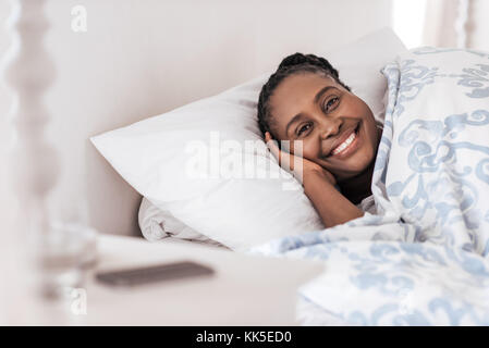 Souriante jeune femme africaine se réveillant dans son lit Banque D'Images