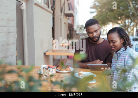 Jeune couple la navigation en ligne à un sidewalk cafe Banque D'Images