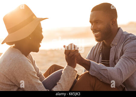 African couple romantique assis ensemble sur une plage au coucher du soleil Banque D'Images