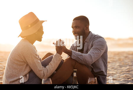 Smiling young couple assis sur une plage au crépuscule Banque D'Images