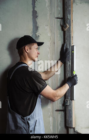 L'homme saisit les chapistes pour aligner le coin du mur Banque D'Images