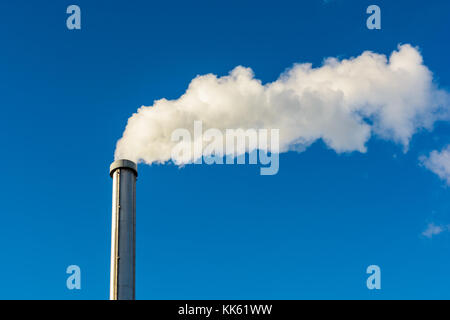 Un long nuage de fumée blanche s'échappant d'un cheminée métallique contre un ciel bleu profond. Banque D'Images